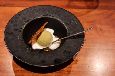 Soğuk yeşil çaylı dondurmayı yanına çıtır bisküvi ve çay kaşığıyla siyah bir tabakta krema ile kapat.