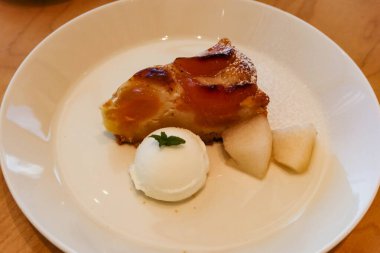 Yanında vanilyalı dondurma olan elmalı turtayı kapayın. Beyaz bir tabakta iki parça armut olsun.