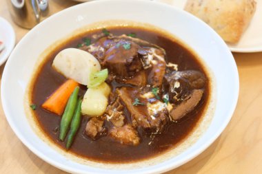 sığır eti ve karışık sebze (turp, havuç, lahana, yeşil fasulye) patatesi üzerine koyu çorba sosu güveci ile beyaz bir tabakta ve yanında daldırmak için ekmek