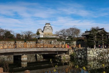 Himeji Şatosu, Himeji, Japonya - 12 Aralık 2024: Eski Himeji şatosunun dış yüzeyi, güneşli bir günde, alçak açılı bir köprüden ve yansımalı bir nehirden fotokopi uzayı. 