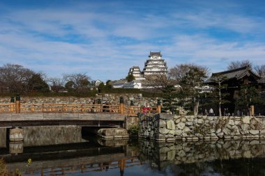 Himeji Şatosu, Himeji, Japonya - 12 Aralık 2024: Eski Himeji şatosunun dış yüzeyi, güneşli bir günde, alçak açılı bir köprüden ve yansımalı bir nehirden fotokopi uzayı. 