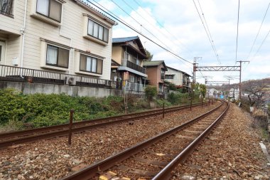 Onomichi, Hiroshima, Japan- 9 Dec 2024: train passing by the railway track outdoor with cables hanging and houses on the other side clipart