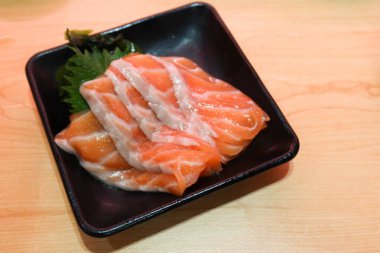 Somon balığını siyah bir tabakta dilimle ve ahşap masada kopya alanı olsun.