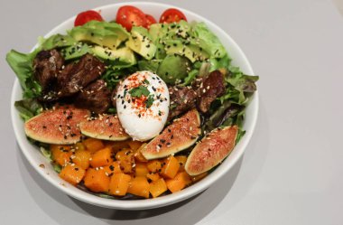 Haşlanmış yumurta, balkabağı, sığır eti parçaları, avokado, lahana ve çeşitli sebze salatasını beyaz kasede siyah ve beyaz susamlı.