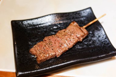 Japon usulü ızgara sığır eti diliyle siyah bir tabakta şiş.