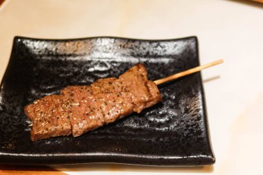 Japon usulü ızgara sığır eti diliyle siyah bir tabakta şiş.
