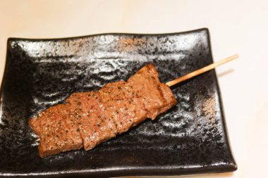 Japon usulü ızgara sığır eti diliyle siyah bir tabakta şiş.