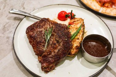 Yanında ananas ve kiraz domatesli ızgara biftek ve beyaz tabakta barbekü sosu sosu.