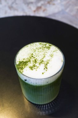 Soğuk buzlu sütlü yeşil çay sütlü sütlü sütlü sütlü sütlü sütlü sütlü sütlü sütlü sütlü sütlü sütlü sütlü sütlü sütlü sütlü sütlü sütlü sütlü sütlü sütlü sütlü sütlü sütlü sütlü sütlü sütlü kahve tozu siyah bir masada şeffaf bir bardakta.