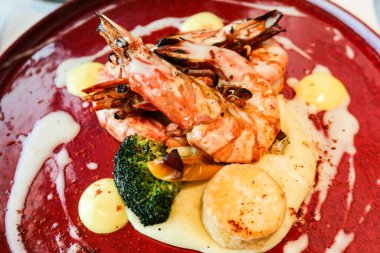 Izgara büyük karidesi deniz tarağıyla kapatın. Brokoli ve patates püresi kırmızı tabakta.