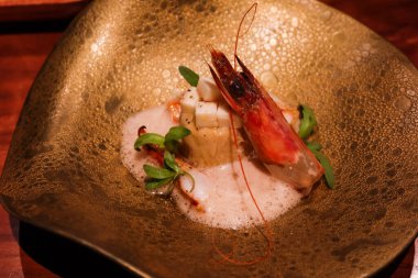 Çiğ saşimi karides, taleggio peyniri, tatlı patates soslu tart ve altın bir tabakta koyu bira köpüğü.