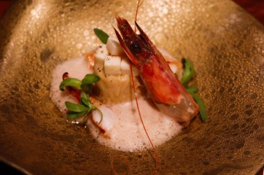 Çiğ saşimi karides, taleggio peyniri, tatlı patates soslu tart ve altın bir tabakta koyu bira köpüğü.