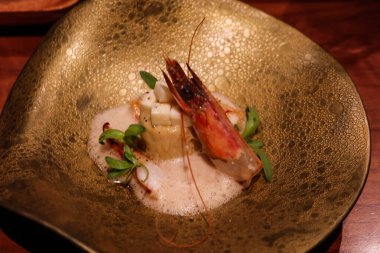 Çiğ saşimi karides, taleggio peyniri, tatlı patates soslu tart ve altın bir tabakta koyu bira köpüğü.