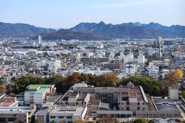 Himeji, Japonya - 12 Aralık 2024: Büyük parkı ve uzun yolu olan şehir manzarası. Himeji Kalesi 'nden gündüz gözüyle iki taraf boyunca binalar