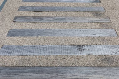 Alternatif ahşap şeritler ve ince, açık renkli çakıllar içeren dokulu yüzey. Ahşap kalaslar yatay olarak seriliyor, doğal tahıllarını sergiliyorlar ve yerde yıpranmış bir görünüm sergiliyorlar.