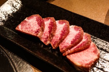 Izgaraya hazır siyah bir tabakta Wagyu sığır dilinin ham dilimini kapat.)
