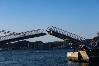 Mojiko, Fukuoka, Japonya - 3 Kasım 2024: geminin gün batımında geçmesi için açılan yaya köprüsü. Sahilde bekleyen Mavi Kanat Moji adındaki insanlar fotokopi alanı ile birlikte.