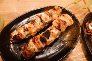 Bir tabakta ızgara tavuk şişi yapan iki Japon yakitori.