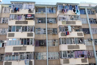 Fuk Loi Malikanesi, Tsuen Wan, Hong Kong - 4 Ocak 2025: Pencereli ve asılmış elbiseli eski bir apartman dairesi. Gündüz vakti dış bina inşa ediliyor