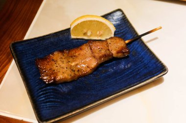 Izakaya restoranında ızgara Japon wagyu sığır eti dili şiş mavi bir tabakta yakitori ve yanında limon dilimi. 