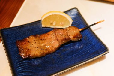 Izakaya restoranında ızgara Japon wagyu sığır eti dili şiş mavi bir tabakta yakitori ve yanında limon dilimi. 