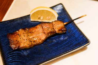 Izakaya restoranında ızgara Japon wagyu sığır eti dili şiş mavi bir tabakta yakitori ve yanında limon dilimi. 