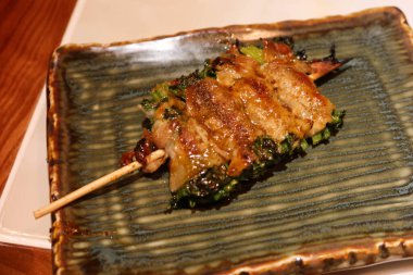 Bir tabakta domuz eti şişi ile sarılmış ızgara soğanı kapat.