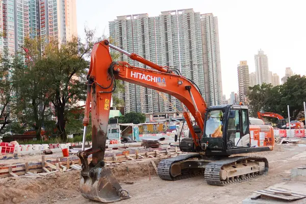 Kai Tak, Hong Kong - 12 Ocak 2025: İnşaat malzemeleri ve ekipmanlarıyla birlikte inşaat alanındaki bir turuncu ve siyah kazıcı 