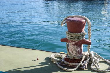 Kırmızı dayanıklı ahşap bir kazık, deniz kıyısında fotokopi alanı olan kalın halatlarla güvenle bağlanmış.