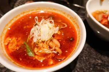 Bir kase Kore kimchi kırmızı baharatlı çorba ince dilimlenmiş yeşil soğan, deniz ürünü ve baharatlı beyaz bir kâse.