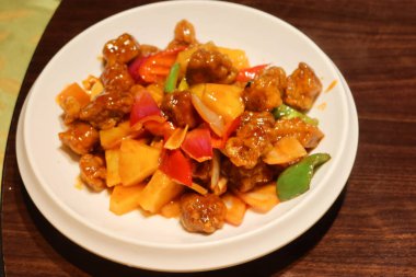 Kanton usulü tatlı ve ekşi domuz eti, ananas, kırmızı ve sarı biberli beyaz tabakta.