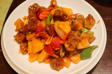 Kanton usulü tatlı ve ekşi domuz eti, ananas, kırmızı ve sarı biberli beyaz tabakta.