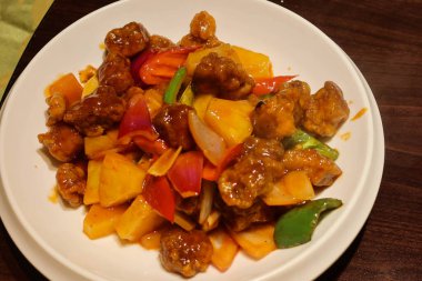 Kanton usulü tatlı ve ekşi domuz eti, ananas, kırmızı ve sarı biberli beyaz tabakta.