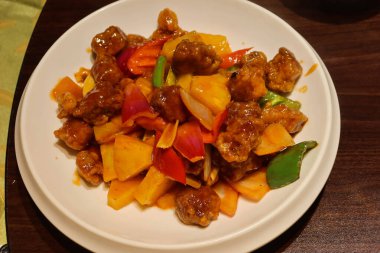 Kanton usulü tatlı ve ekşi domuz eti, ananas, kırmızı ve sarı biberli beyaz tabakta.