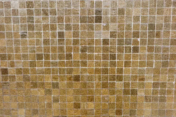 Küçük kare mozaik fayanslardan oluşmuş desenli bir duvarın yakın görüntüsü. Fayanslar, ağırlıklı olarak kahverengi ve bej tonlarında bir dizi sıcak toprak tonu içerir ve arka plan olarak kullanılabilir.