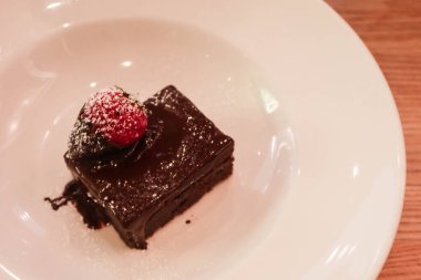 Çikolata soslu çikolatalı brownie 'ye yakın, üstüne de beyaz bir tabakta fotokopi alanı olan çilek.