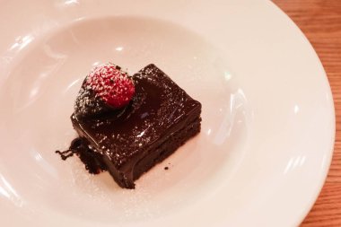Çikolata soslu çikolatalı brownie 'ye yakın, üstüne de beyaz bir tabakta fotokopi alanı olan çilek.