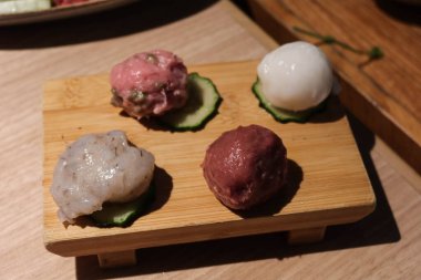 Balık köftesi, kıymalı köfte, köfte ve salatalık dilimlenmiş kalamar köftesi de dahil olmak üzere çiğ haşlanmamış malzeme. Hepsi tahta bir tahtaya yerleştirilmiş..