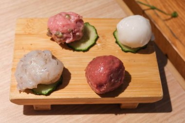 Balık köftesi, kıymalı köfte, köfte ve salatalık dilimlenmiş kalamar köftesi de dahil olmak üzere çiğ haşlanmamış malzeme. Hepsi tahta bir tahtaya yerleştirilmiş..