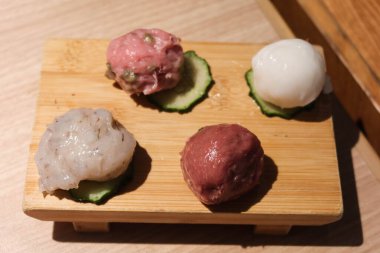 Balık köftesi, kıymalı köfte, köfte ve salatalık dilimlenmiş kalamar köftesi de dahil olmak üzere çiğ haşlanmamış malzeme. Hepsi tahta bir tahtaya yerleştirilmiş..