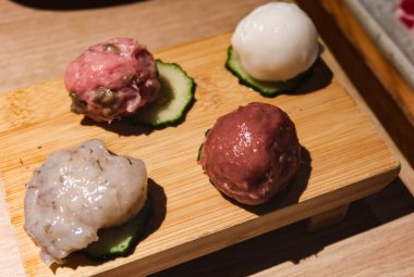 Balık köftesi, kıymalı köfte, köfte ve salatalık dilimlenmiş kalamar köftesi de dahil olmak üzere çiğ haşlanmamış malzeme. Hepsi tahta bir tahtaya yerleştirilmiş..