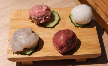 Balık köftesi, kıymalı köfte, köfte ve salatalık dilimlenmiş kalamar köftesi de dahil olmak üzere çiğ haşlanmamış malzeme. Hepsi tahta bir tahtaya yerleştirilmiş..