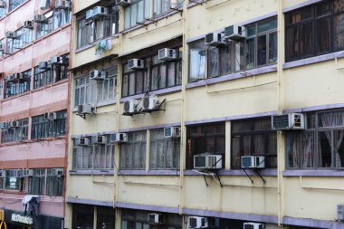 Mongkok, Hong Kong. 28 Ocak 2025. Eski, yırtık bir apartmanın dış cephesi sarıya boyanmış ve duvarında klima asılı. Fotoğraf mahallede alçak bir açıdan çekilmiş..