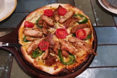 Izgara tavuk parçaları, yeşil biber, vişneli domates ve peynirli pizza servis tahtasının üzerinde.