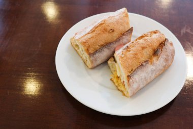 Jambonlu ve peynirli ekmekli sandviçin yarısı beyaz tabakta, fotokopi alanı ile kesilmiş.