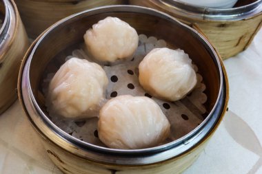 Çin çay evi restoranında beyaz yapraklı çiçekli masa örtüsü olan bir masada bambu buharlı bir tencerede dört parça Hong Kong Dim Sum buğulanmış karides köftesi.