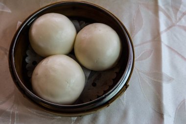 Buharda pişirilmiş üç beyaz Kanton Dim Sum kremalı kremalı çöreği bambu buharlı buharlı tencereye koy.