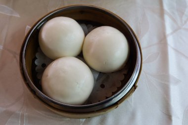 Buharda pişirilmiş üç beyaz Kanton Dim Sum kremalı kremalı çöreği bambu buharlı buharlı tencereye koy.