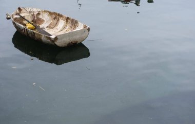Yıpranmış yaşlı bir kayık, sakin suyun üzerinde hafifçe yüzüyor, çatlak ve soyulmuş boyalar, suda yansıyor ve kopyalama alanı var.