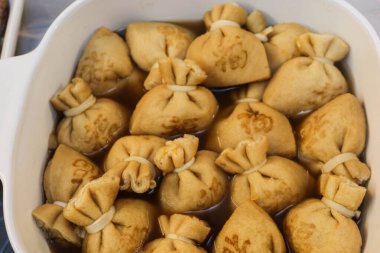 Büyük bir kap haşlanmış Japon tofu (soya peyniri) kesesine yakın pirinç keki (mochi kinchaku) ve Japonca bir kelime olan 